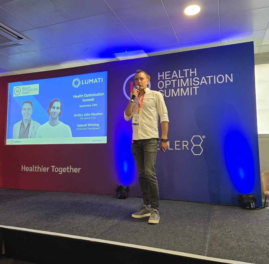 Ashley Heather speaking into a microphone on stage during a presentation at the Health Optimisation Summit.